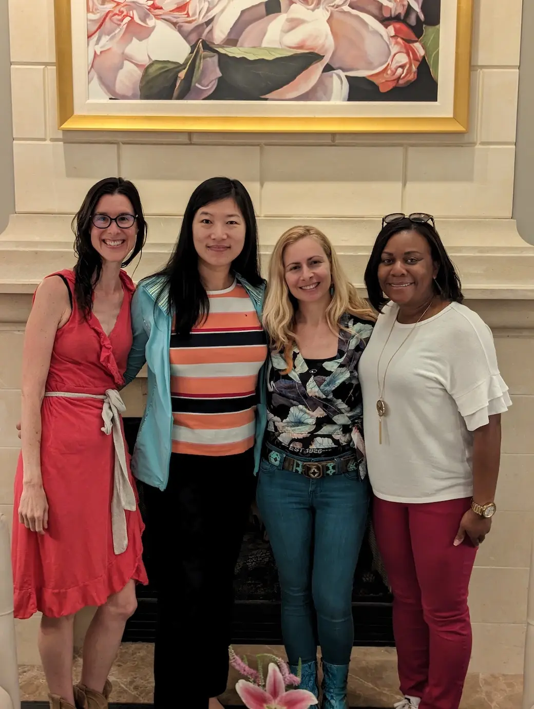 Four women posing in front of a fireplace standing shoulder to shoulder smiling.